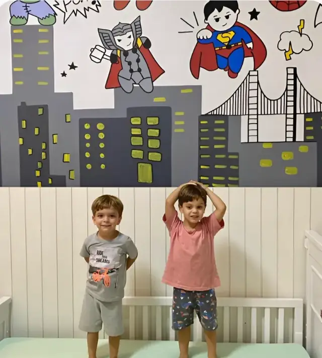 Dois meninos em pé na cama diante de um mural de super-heróis
